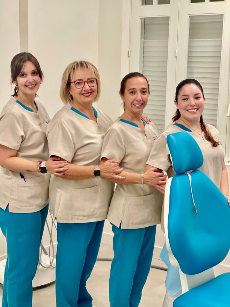 Nuestro Equipo Profesional: Grupo de auxiliares y personal de la clínica posando con uniforme junto a un sillón dental azul.