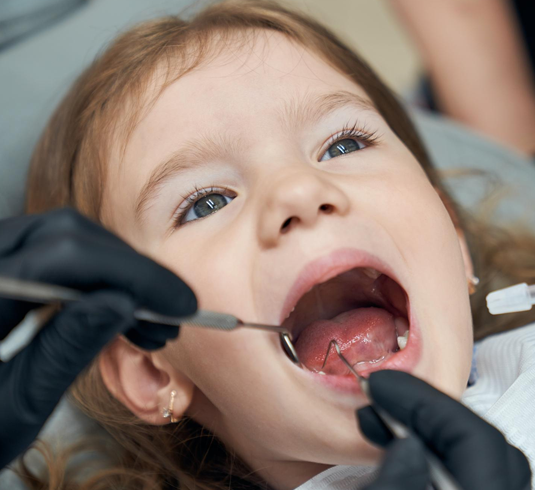 Odontopediatra examinando los dientes de una niña durante una revisión de salud bucal.